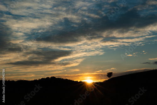 Obraz na płótnie sagome nere di colline ed alberi in primo piano con cielo nuvoloso al tramonto, colorato di arancione w salonie