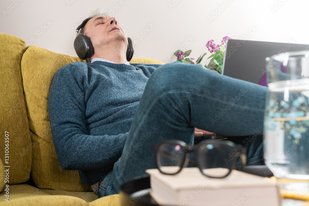 Obraz premium Man relaxing on couch with headphones, listening to music and unwinding