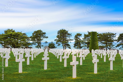Rows of white cross grave markers dotted with manicured hedges in the American Cemetery in Caen, Normandy, France