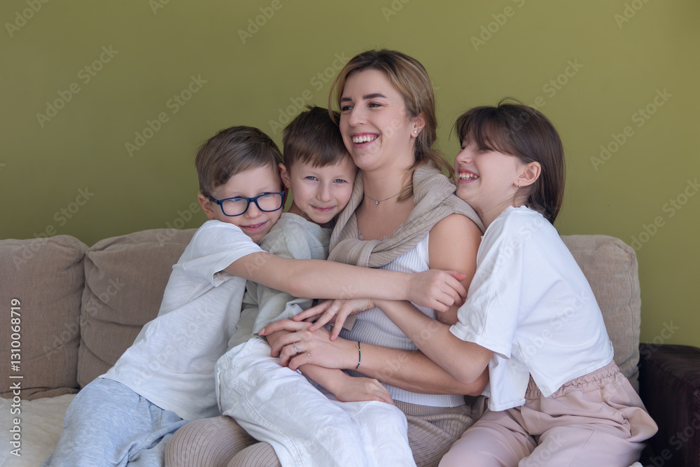 Happy mother hugging her three children. A joyful mother sits on a couch, embracing her three smiling children in a warm and loving family moment against a green wall. Happy mother hugging her three children. A joyful mother sits on a couch, embracing her three smiling children in a warm and loving family moment against a green wall.