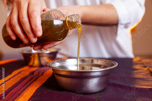  pouring warm oil from a bottle into a bowl for traditional  massage image suitable for yoga, medical, masseur, therapy and body care photo