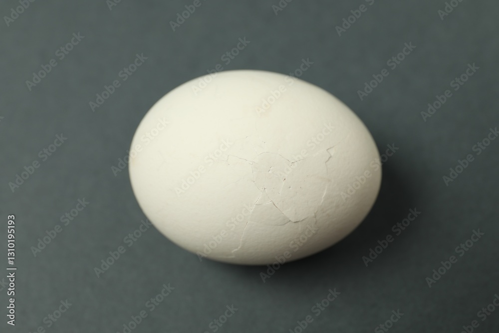 One egg with cracked shell on grey background, closeup One egg with cracked shell on grey background, closeup