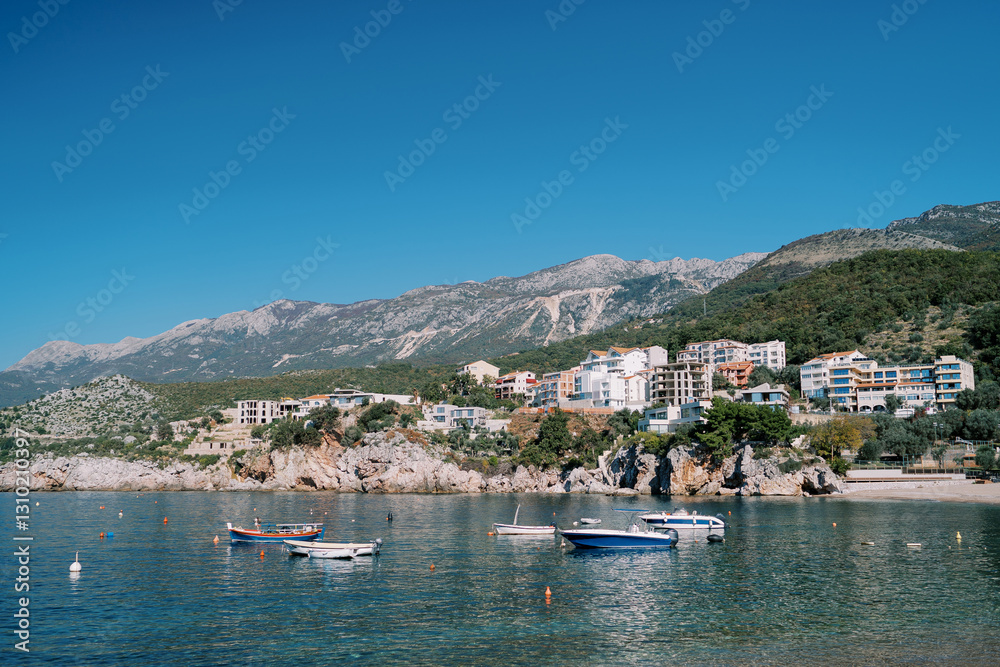 Obraz premium Fishing boats are moored in the sea near colorful hotels on a rocky slope. Przno, Montenegro
