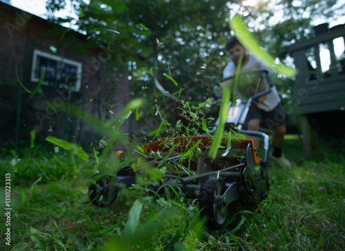 Grass clippings flying, man uses push reel lawn mower to cut grass in yard