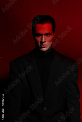 Close Up portrait of a handsome serious young man in black suit over red dark background. Horizontal view. Space for text.