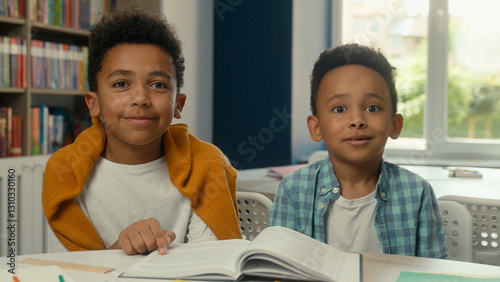 African American little boys siblings pupils schoolboys children kids students studying at desk school primary education reading book in library prepare lesson looking at camera smiling cute faces