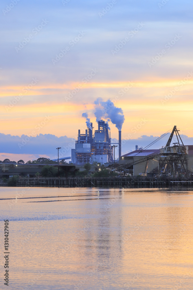 Fototapeta premium An expansive factory complex illuminated by the golden glow of a tropical sunset, surrounded by dense forest, June 25, 2019, highlighting industry coexisting with wild nature, location unspecified
