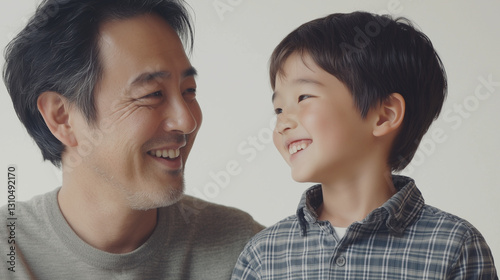 Obraz na płótnie 日本人の父と子が向かい合って微笑みあっている。スタジオ撮影の背景白。五歳、6歳の幼児の男の子と40代の父親。上半身 w salonie