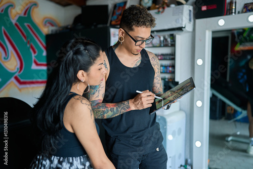 Professional tattoo artist reviewing design on digital tablet with client inside modern studio