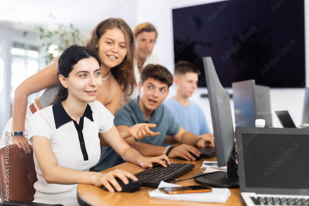 Obraz premium Friendly young students, girls and guys, actively involved in collaborative learning, sitting around table in computer lab excitedly discussing class project or engaging in group study session