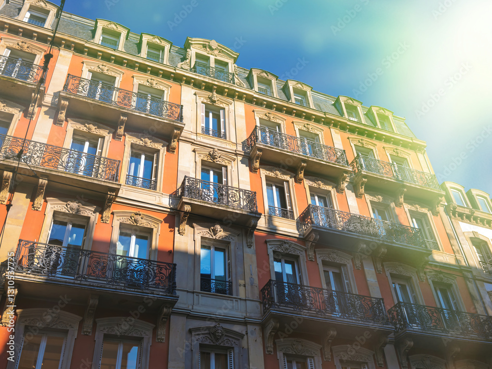 Fototapeta premium Sunlit traditional European building showcases ornate balconies and vibrant facades under a clear blue sky.