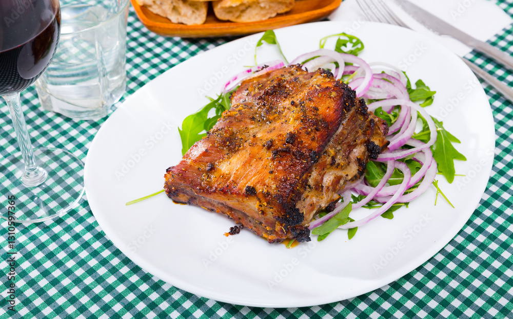 Baked pork ribs baked served at plate with salad from arugula and onion Baked pork ribs baked served at plate with salad from arugula and onion