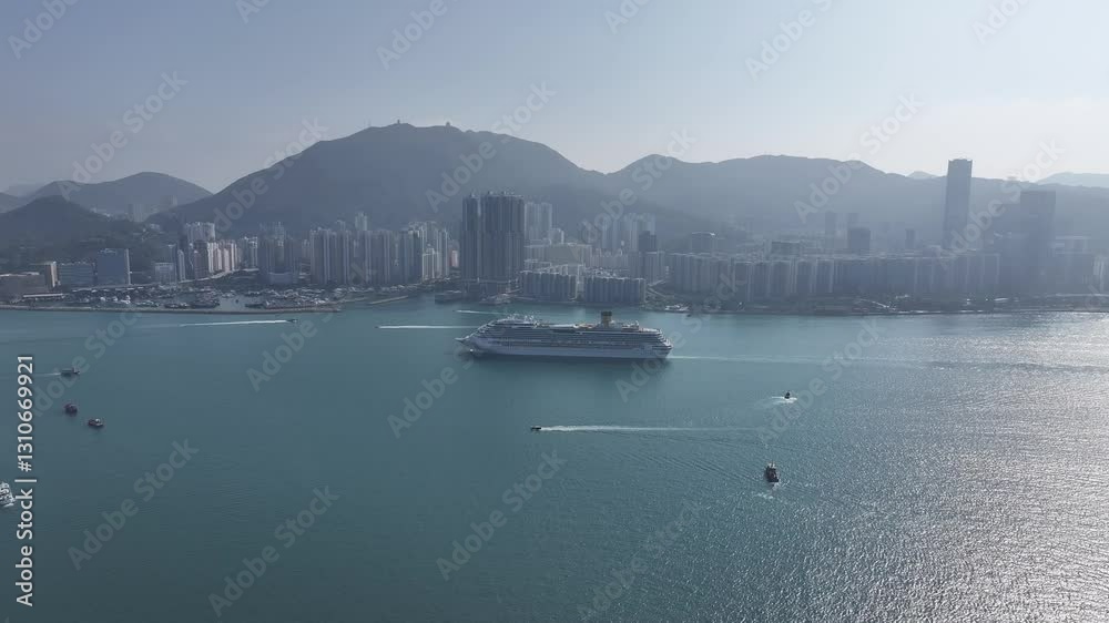 Drone aerial skyview of a mega luxury cruise ship sailing at the Kai Tak cruise terminal, showcasing the vibrant Victoria Harbour and the iconic city skyline of Kwun Tong Kowloon Hong Kong Drone aerial skyview of a mega luxury cruise ship sailing at the Kai Tak cruise terminal, showcasing the vibrant Victoria Harbour and the iconic city skyline of Kwun Tong Kowloon Hong Kong