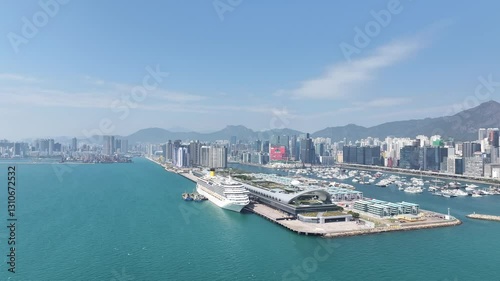 Drone aerial skyview of a mega luxury cruise ship sailing at the Kai Tak cruise terminal, showcasing the vibrant Victoria Harbour and the iconic city skyline of Kwun Tong Kowloon Hong Kong 