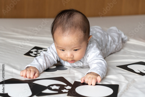 5 month old baby playing with picture cards on the bed in the morning.