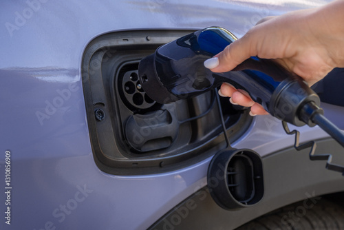 A woman's hand charges a purple EV electric car