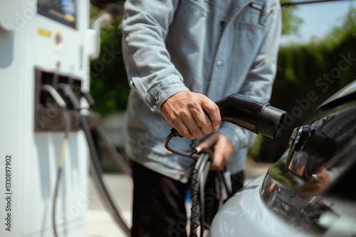 Person charging an electric vehicle at a charging station on a sunny day in a green outdoor setting