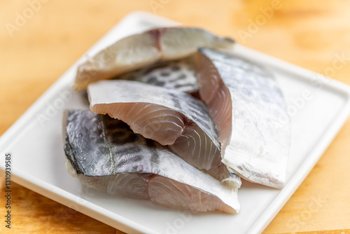 透き通るような身の鮮度が際立つ、旬の「サワラ（鰆）の切り身」。西京焼きや塩焼き、ムニエルなど幅広い料理に使える素材は、鮮魚店の販促広告、和食メニューの素材紹介、旬の魚介レシピのイメージに最適な高品質素材です。 | Fresh sliced Spanish mackerel (Sawara) fillets on a white plate.