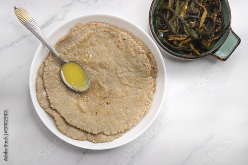 Jowar flour flatbread known as bhakar or jawari bhakri. served with ghee, spicy garlic or lasun chutney, bhindi or lady finger sabji. farmer's food. Maharashtrian village food. copy space. photo