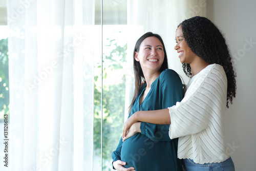 Happy interracial lesbian couple looking each other enjoying pregnancy