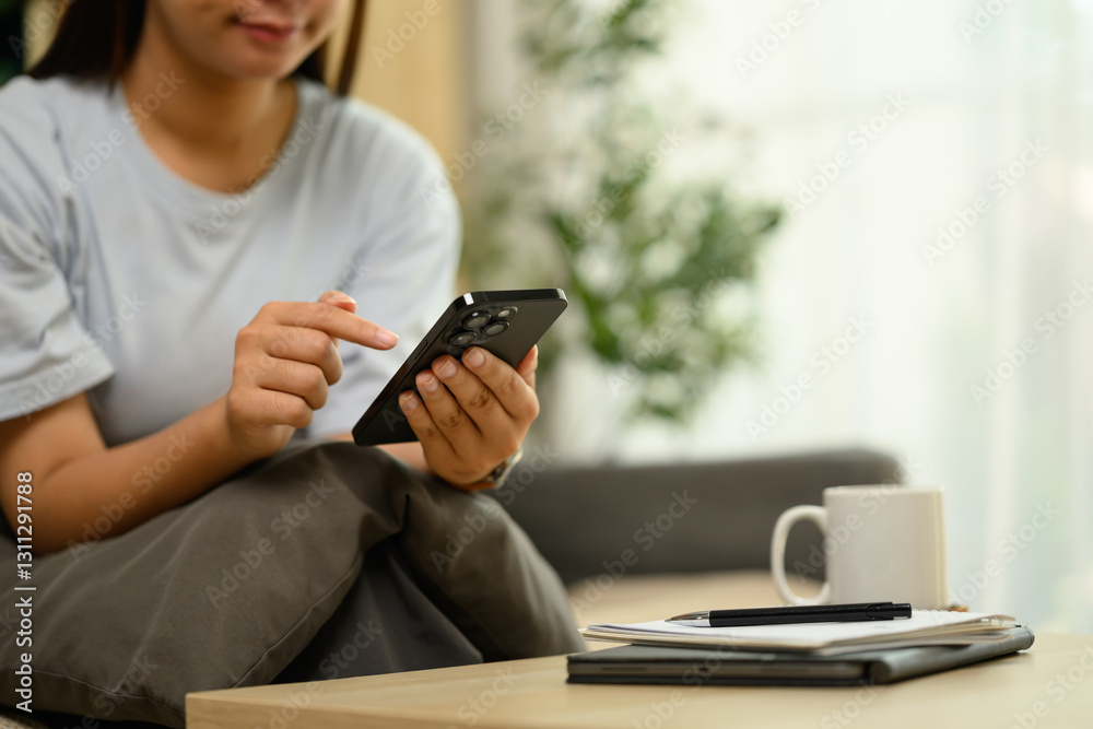 Cropped shot young woman in casual clothes using mobile phone on sofa