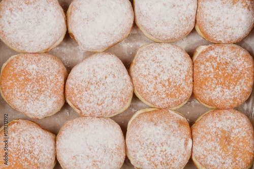 A detailed overhead shot of freshly baked doughnuts sprinkled with powdered sugar, arranged in rows on a light surface photo