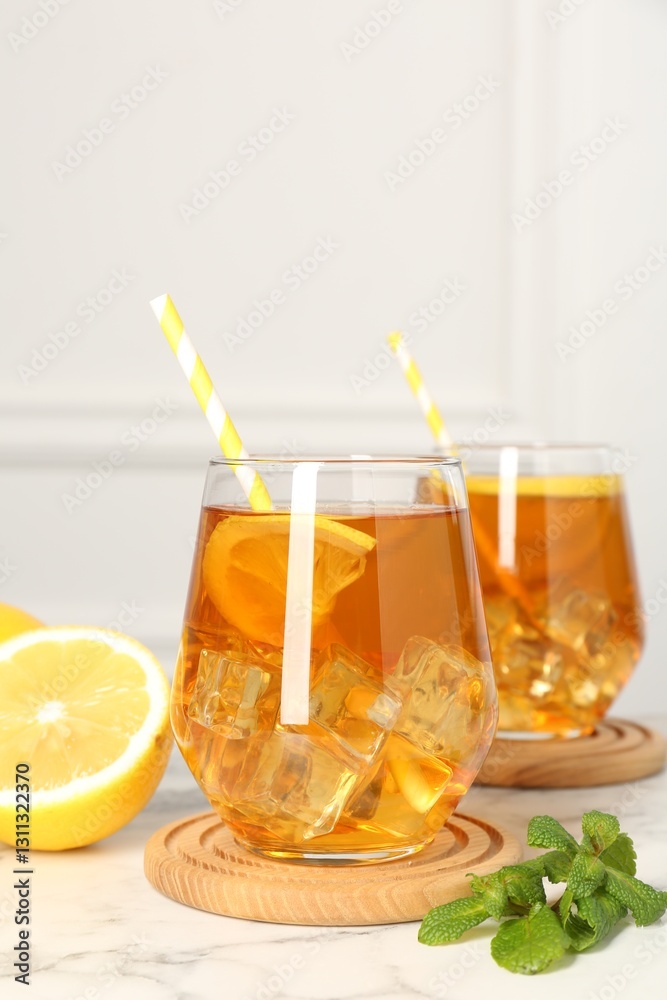 Fototapeta premium Refreshing iced tea with slices of lemon, mint and drinking straws on white marble table, closeup