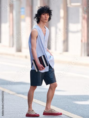 Portrait of handsome Chinese young man wearing undershirt and shorts posing in the street, young guy with black curly hair with urban background. male fashion, cool Asian young man lifestyle.