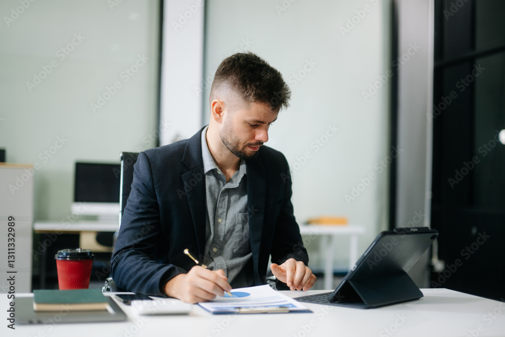 Confident businessman working on finance analysis with a tablet and laptop at office desk. professional workplace concepts.. Confident businessman working on finance analysis with a tablet and laptop at office desk. professional workplace concepts..