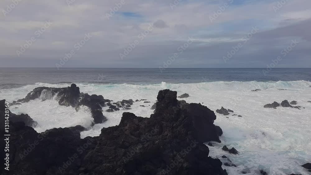 Playful waves of the Atlantic Ocean crash against the rugged volcanic rock formations of the Azores Islands under a dark cloudy sky Playful waves of the Atlantic Ocean crash against the rugged volcanic rock formations of the Azores Islands under a dark cloudy sky