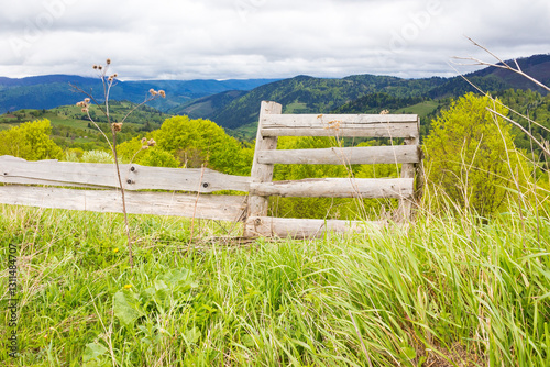 Obraz na płótnie wooden fence near meadow on the hill. mountainous rural landscape of transcarpathia in spring. beautiful view of countryside with grass on field and forested on hillside beneath a cloudy sky w salonie