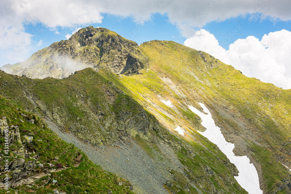 landscape of fagaras mountains in summer. beautiful nature scenery of romania. steep slope, grassy hillside and rocky peak on a sunny day with clouds on the blue sky. scenic travel background