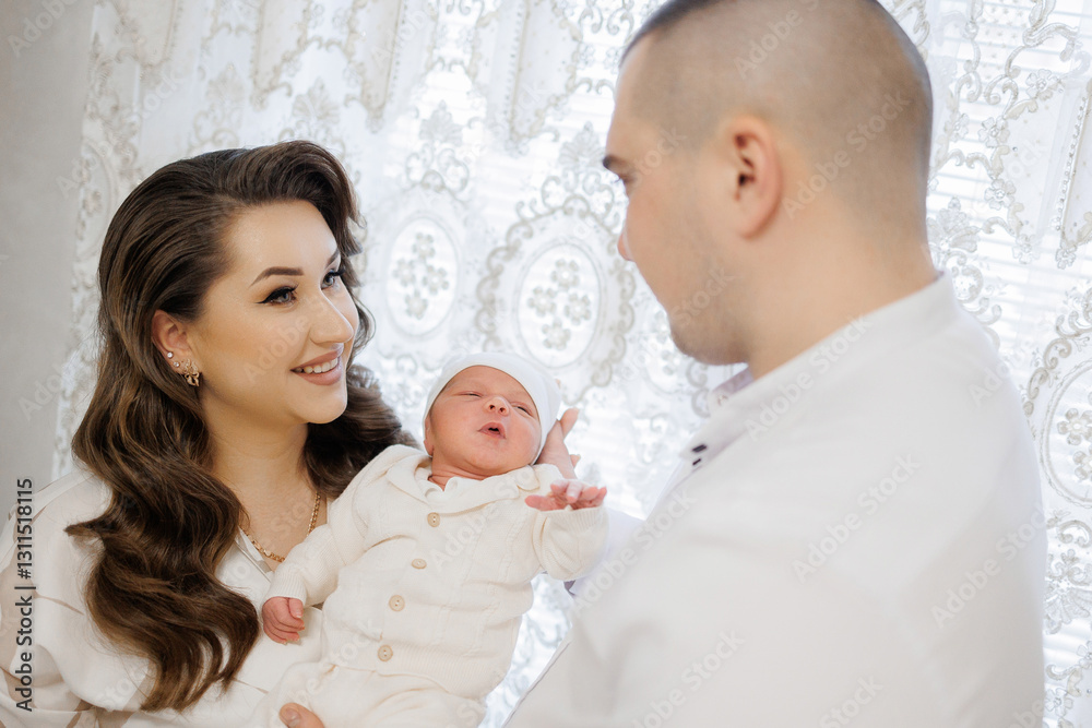 A man and a woman are holding a baby. The baby is wearing a white outfit. Scene is happy and joyful A man and a woman are holding a baby. The baby is wearing a white outfit. Scene is happy and joyful