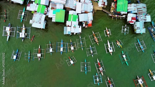 Stunning top-down aerial view rising above a traditional Filipino fishing village in Puerto Princesa, Palawan Island, capturing vibrant boats, colorful roofs, and authentic coastal lifestyle.
