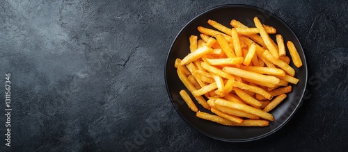 Crispy homemade French fries in a black round bowl on a dark textured surface, top view showcasing golden color and ample copy space on the side
