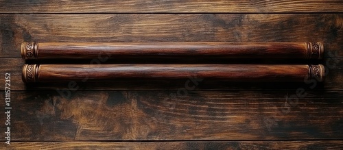 Two traditional wooden nunchaku weapons arranged horizontally on a rustic brown wooden surface showcasing intricate detailing and craftsmanship. photo