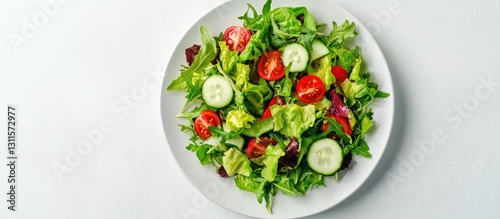 Fresh vibrant mix of green salad leaves with cherry tomatoes and cucumber slices arranged on a white plate top view against a plain background