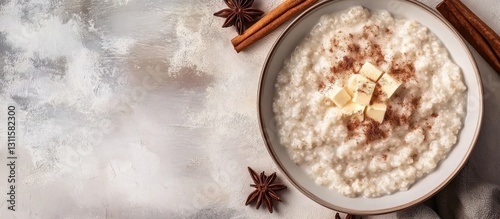 Creamy rice porridge topped with butter and cinnamon in a white ceramic bowl on a light textured background with star anise and cinnamon sticks