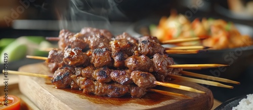 Indonesian lamb satay skewers on a wooden board with smoke rising, surrounded by vibrant side dishes and vegetables, showcasing rich browns and greens.