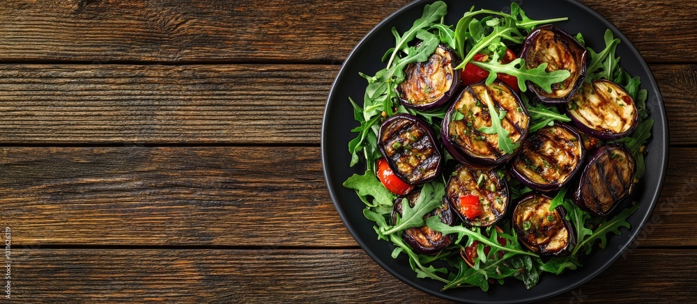 Roasted eggplant and arugula salad in a black bowl on a wooden table with warm tones and empty space for text on the left side Roasted eggplant and arugula salad in a black bowl on a wooden table with warm tones and empty space for text on the left side
