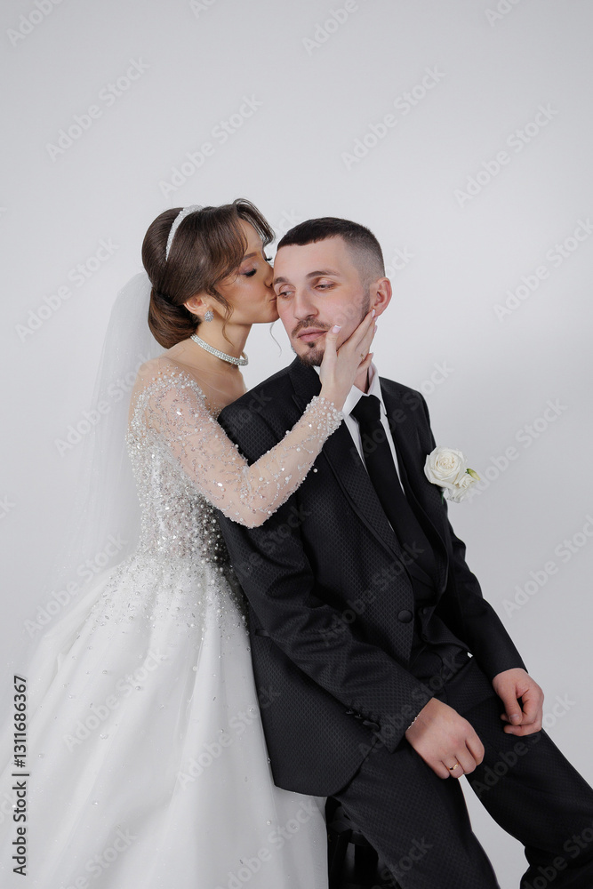 A bride and groom are kissing each other's necks. The bride is wearing a white dress and the groom is wearing a black suit A bride and groom are kissing each other's necks. The bride is wearing a white dress and the groom is wearing a black suit