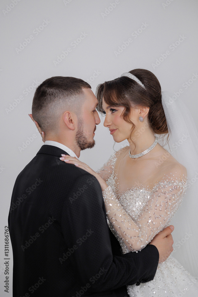 A bride and groom are embracing each other in a wedding photo. The bride is wearing a beautiful dress with a large pearl necklace. The man is wearing a suit and tie A bride and groom are embracing each other in a wedding photo. The bride is wearing a beautiful dress with a large pearl necklace. The man is wearing a suit and tie