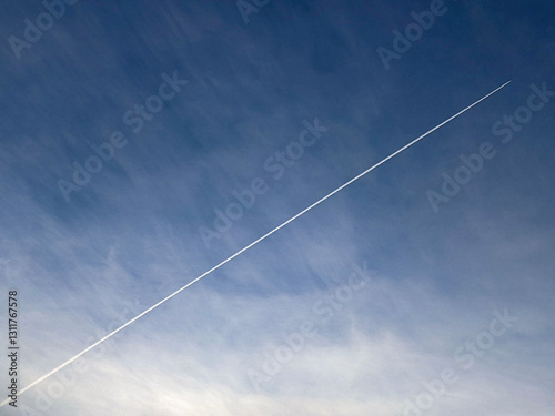 A contrail left by an aircraft streaking across the tranquil azure sky with cirrus clouds. Captures movement and serenity in an expansive atmospheric scene with a forest below