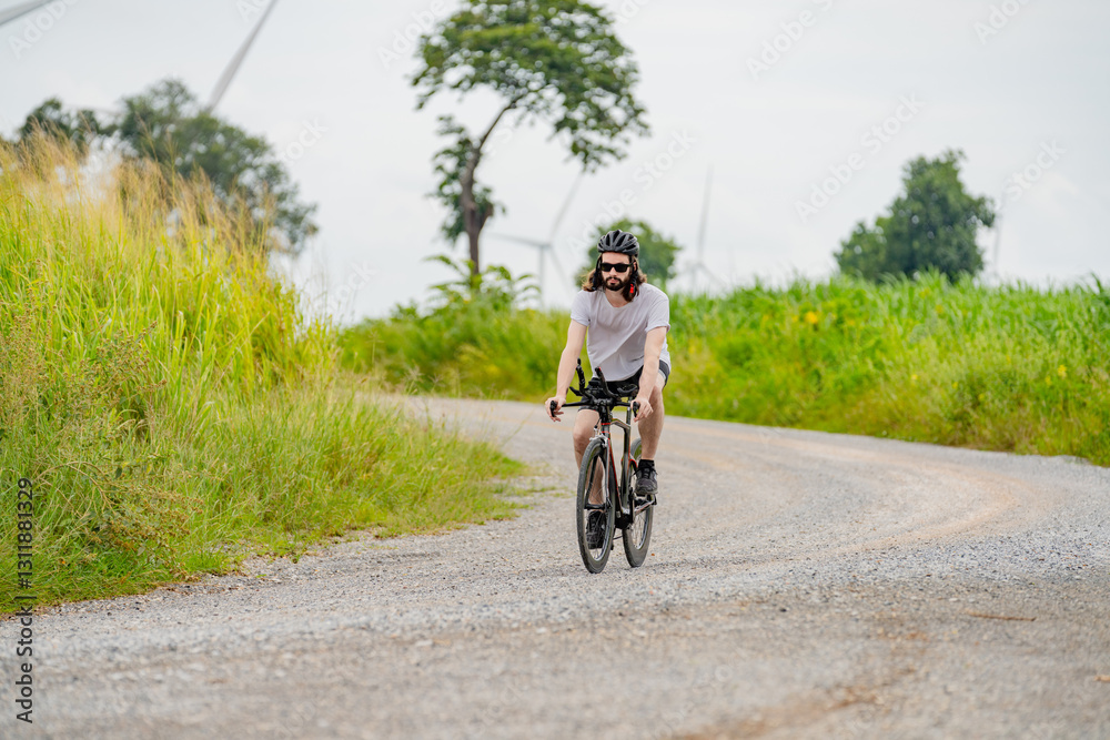 Bicyclist navigating a gravel path surrounded by greenery and wind turbines on a cloudy day Bicyclist navigating a gravel path surrounded by greenery and wind turbines on a cloudy day