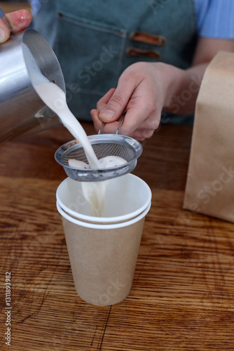 Female barista pouring milk chai drink into cup on a cafe benchtop photo