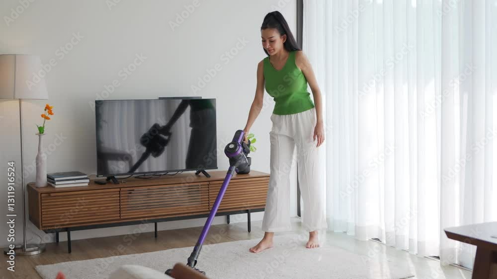 Asian woman engages in cleaning activities in a well-lit, modern living room. She uses a vacuum cleaner while maintaining a tidy environment filled with plants and contemporary furniture Asian woman engages in cleaning activities in a well-lit, modern living room. She uses a vacuum cleaner while maintaining a tidy environment filled with plants and contemporary furniture