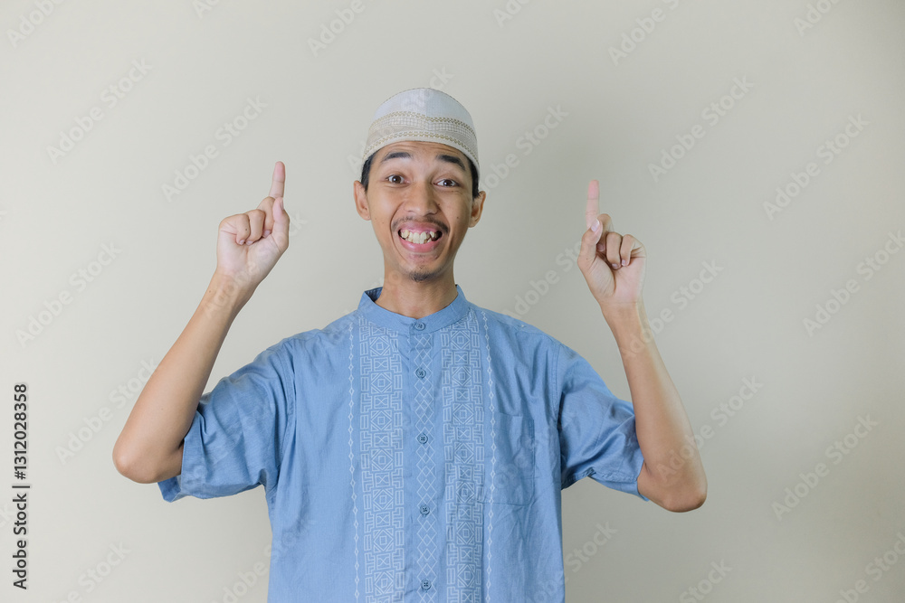 Asian Muslim man smiling cheerfully while looking and pointing to copy space upside her, standing on isolated white background Asian Muslim man smiling cheerfully while looking and pointing to copy space upside her, standing on isolated white background