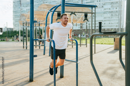 A man exercises energetically on parallel bars in an outdoor urban gym, enjoying a sunny day with a backdrop of modern city buildings.