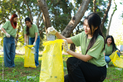 Asian female volunteer team helps society by collecting plastic waste on the grass and putting it in yellow bags to help maintain cleanliness in public areas. World Environment Day CSR