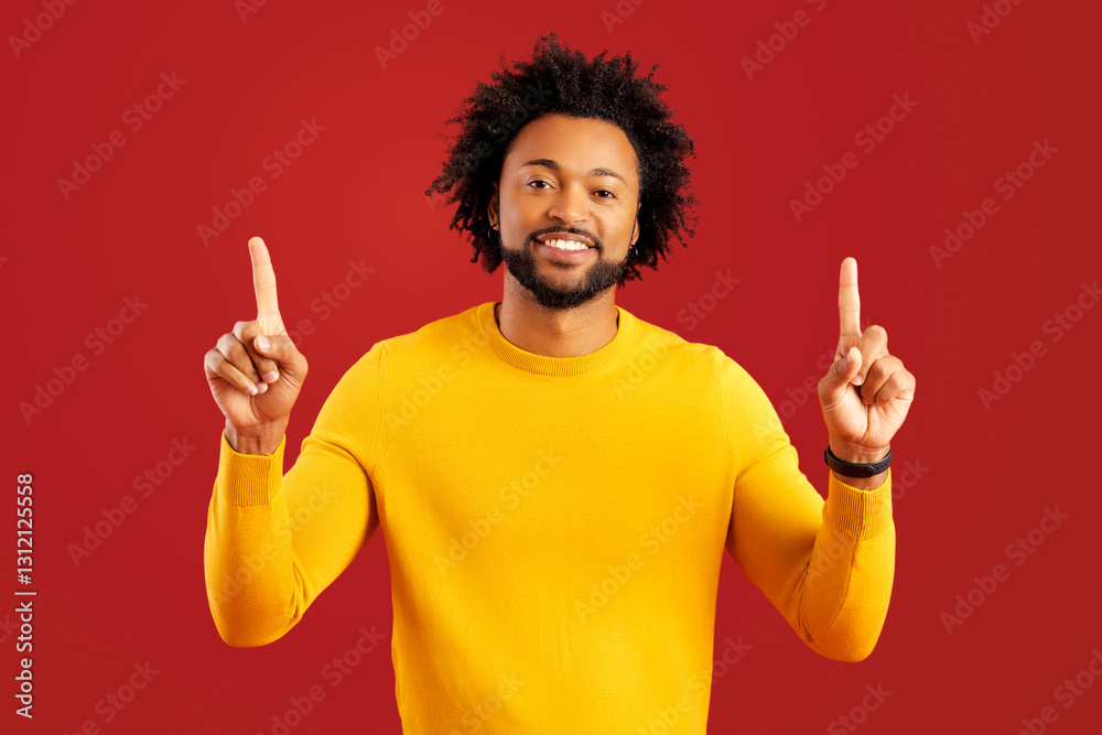 Attractive curly man with overjoyed facial expression pointing up with both fingers, presenting copy space. Indoor studio shot isolated on red background Attractive curly man with overjoyed facial expression pointing up with both fingers, presenting copy space. Indoor studio shot isolated on red background